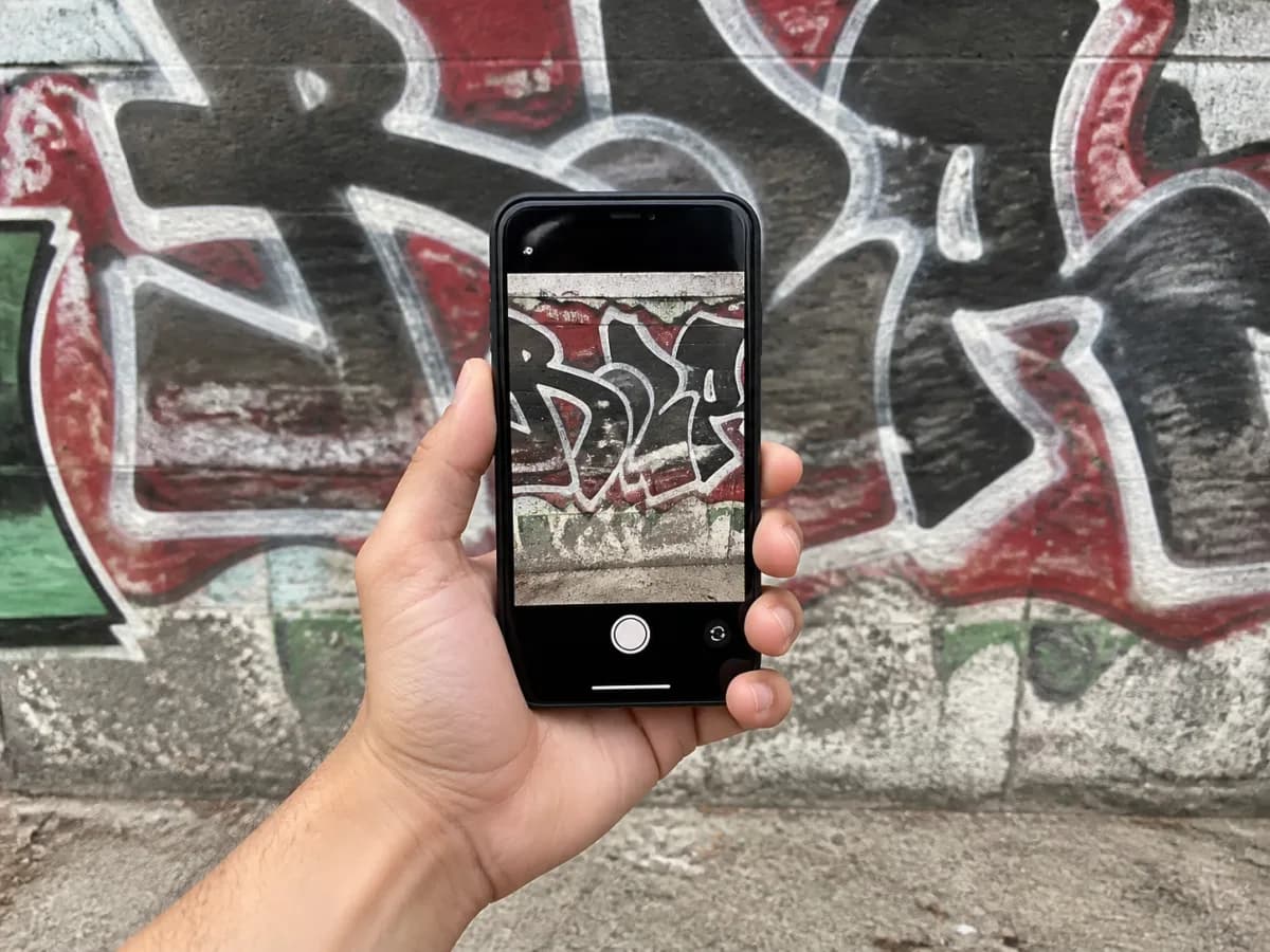 Klient fotografuje posprejovanou zeď telefonem na výšku